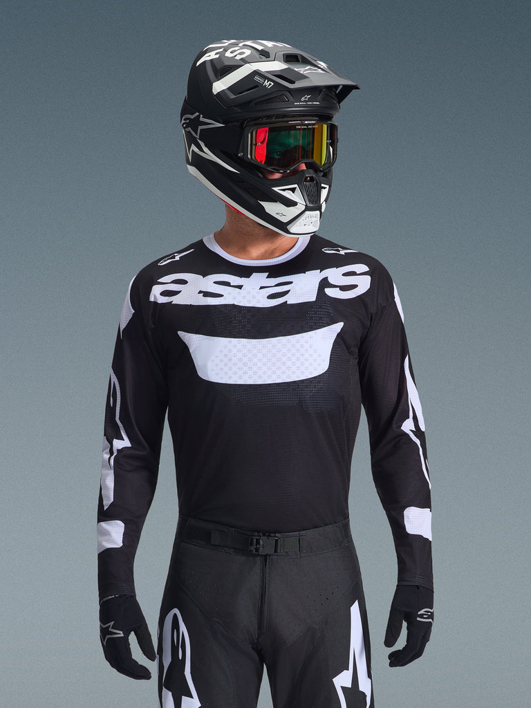 Alpinestars 2026 Racer Air Riway Jersey, schwarz-weißes Motocross-Trikot mit 'astars'-Branding, getragen von einem Fahrer mit passendem schwarzem Helm, Goggles und Hose, mit atmungsaktiven Mesh-Einsätzen für den Offroad-Rennsport.
