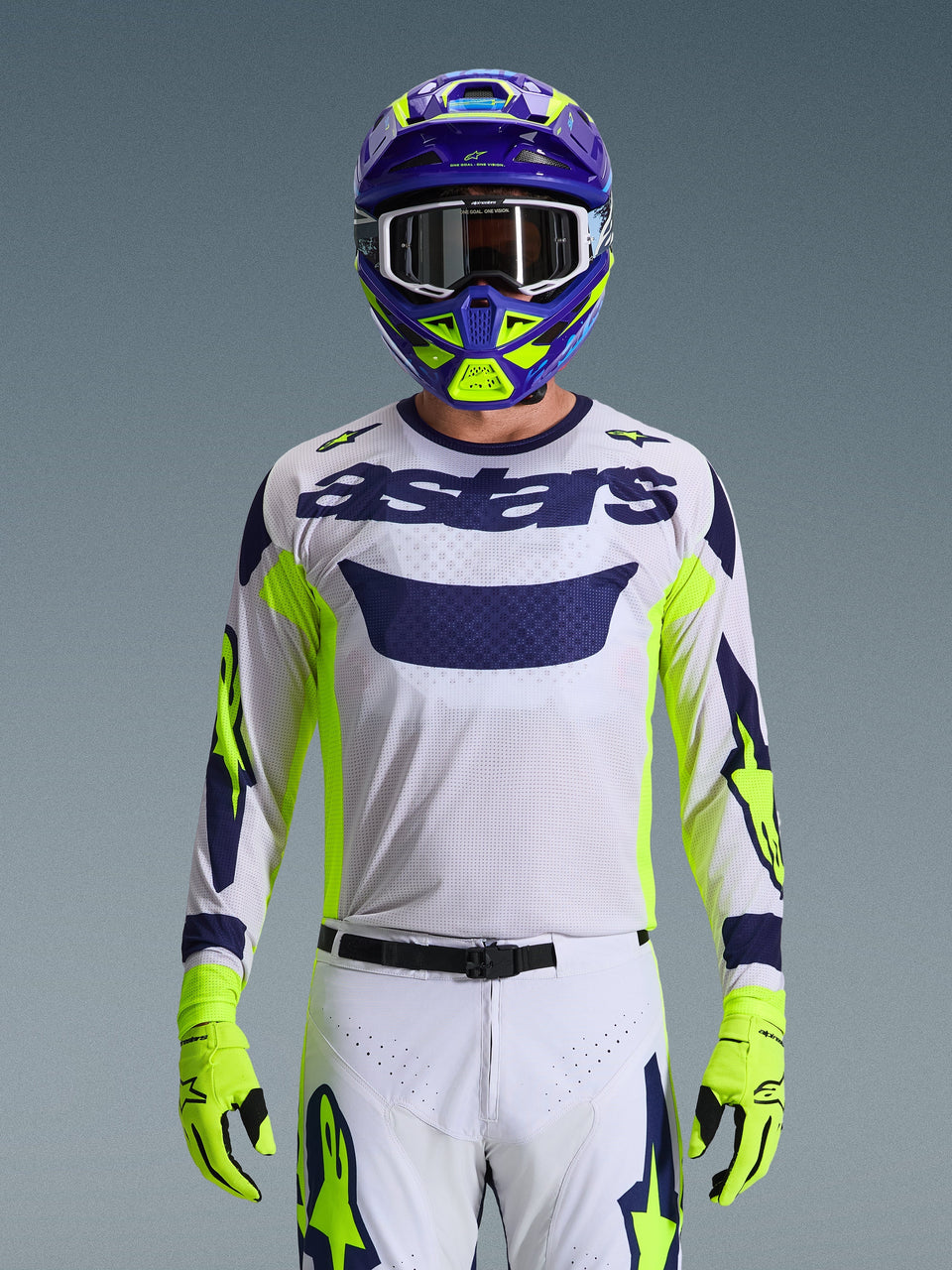 Alpinestars 2026 Racer Air Riway Jersey, Light Gray with Dark Blue astars logo, Fluo Yellow and Blue accents on sleeves, worn by a motocross rider with matching purple and neon yellow helmet and gloves, technical mesh fabric for off-road racing.
