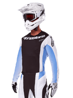 Motocross rider wearing Alpinestars 2025 Techstar Melt Gear Set, White with black and light blue accents, featuring a jersey with a black chest and white sleeves, matching white and black pants, white SM10 helmet with goggles, and black and white gloves, complete professional off-road racing outfit.