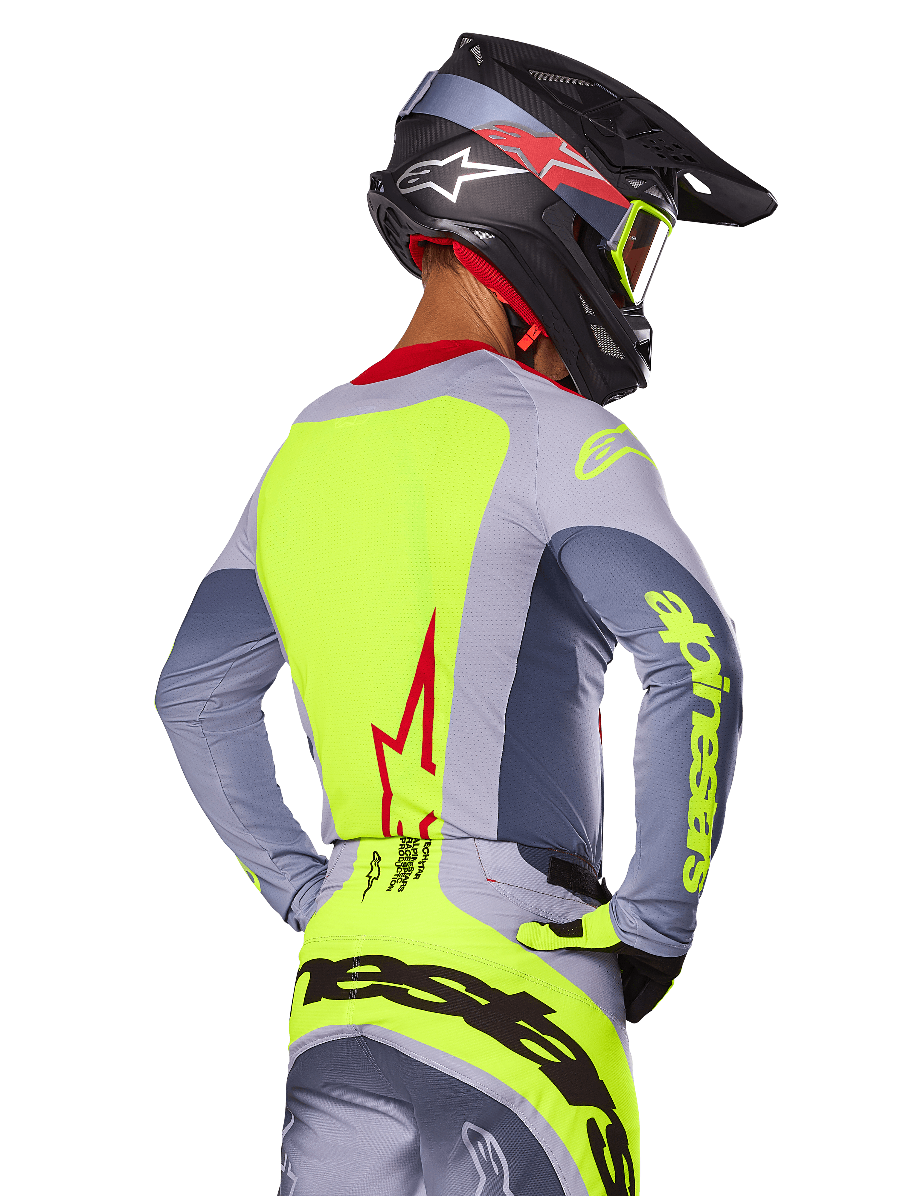 Maillot Alpinestars Techstar Melt 2025, Rouge Vif Gris, vue arrière d'un pilote de motocross portant une tenue de course grise et jaune fluo, logo étoile rouge dans le dos, casque noir et rouge assorti, équipement tout-terrain haute performance