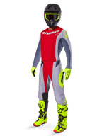 Pilote de motocross portant le maillot Alpinestars Techstar Melt 2025 rouge vif et gris, avec buste rouge et manches grises aux accents jaune fluo, assorti d'un pantalon coordonné, de bottes et gants jaune vif, et d'un casque noir avec lunettes à monture jaune pour une tenue de course tout-terrain complète.