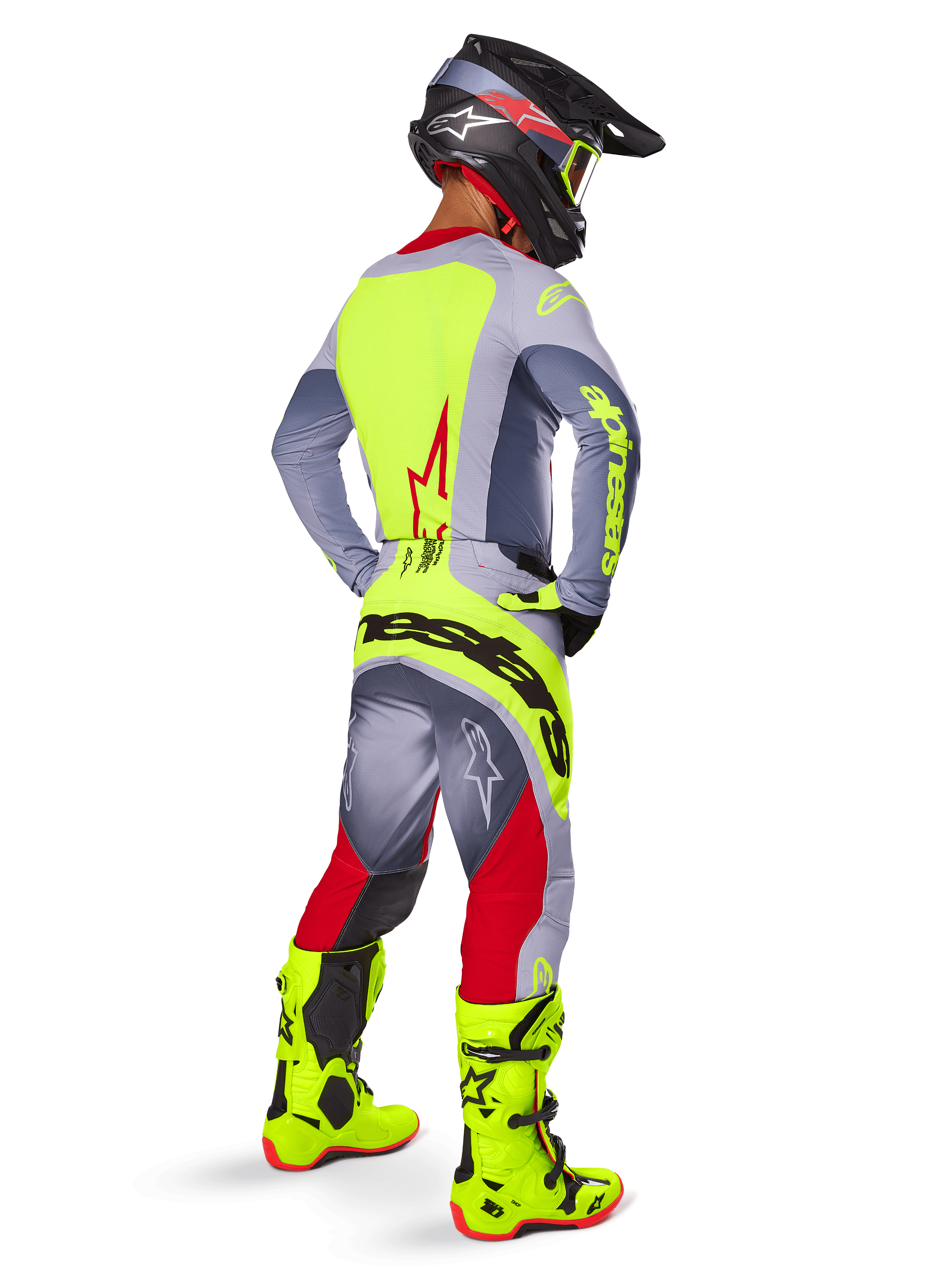 Pilote de motocross vu de dos portant le maillot Alpinestars Techstar Melt 2025 en rouge et gris, avec panneau arrière jaune vif et manches grises, pantalon assorti gris et rouge avec logos jaunes, bottes de motocross jaune vif et casque noir avec lunettes jaunes, tenue de course tout-terrain coordonnée