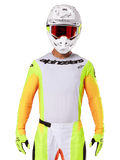 Alpinestars 2025 Techstar Melt Trikot, Motocross-Rennbekleidung, weiße Brust mit neongelben und orangen Ärmeln, Fahrer mit weißem Helm und roter Brille, neongelbe Handschuhe mit schwarzen Logos, lebendige Farbkombination für Offroad-Performance