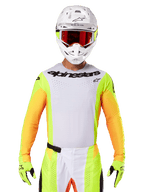 Alpinestars 2025 Techstar Melt Jersey, motorcross racekleding, wit borststuk met neongele en oranje mouwen, rijder draagt witte helm en rode bril, neongele handschoenen met zwarte logo's, levendige kleurstelling voor off-road prestaties