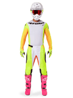 Alpinestars 2025 Techstar Melt Trikot, Motocross-Fahrer in kompletter Ausrüstung, weiß-gelbes Trikot mit orangenen Ärmeln, passende gelbe Hose, leuchtend pinke Stiefel, weißer Helm mit roter Schutzbrille, abgestimmte Offroad-Rennausrüstung