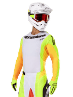 Motorcrosser in Alpinestars 2025 Techstar Melt gearset, wit jersey met felgele en oranje mouwen, zwarte 'Alpinestars' merknaam op de borst, bijpassende neongele handschoenen, witte helm met roodgetinte crossbril, professionele off-road race-uitrusting