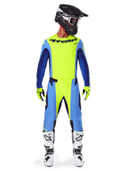 Pilote de motocross portant une tenue de course complète, maillot Alpinestars Techstar Melt 2025 jaune fluo et bleu, pantalon de motocross jaune et bleu assorti, casque noir avec graphismes blancs et lunettes, bottes blanches et noires, gants jaunes et noirs, tenue de performance coordonnée pour la course tout-terrain