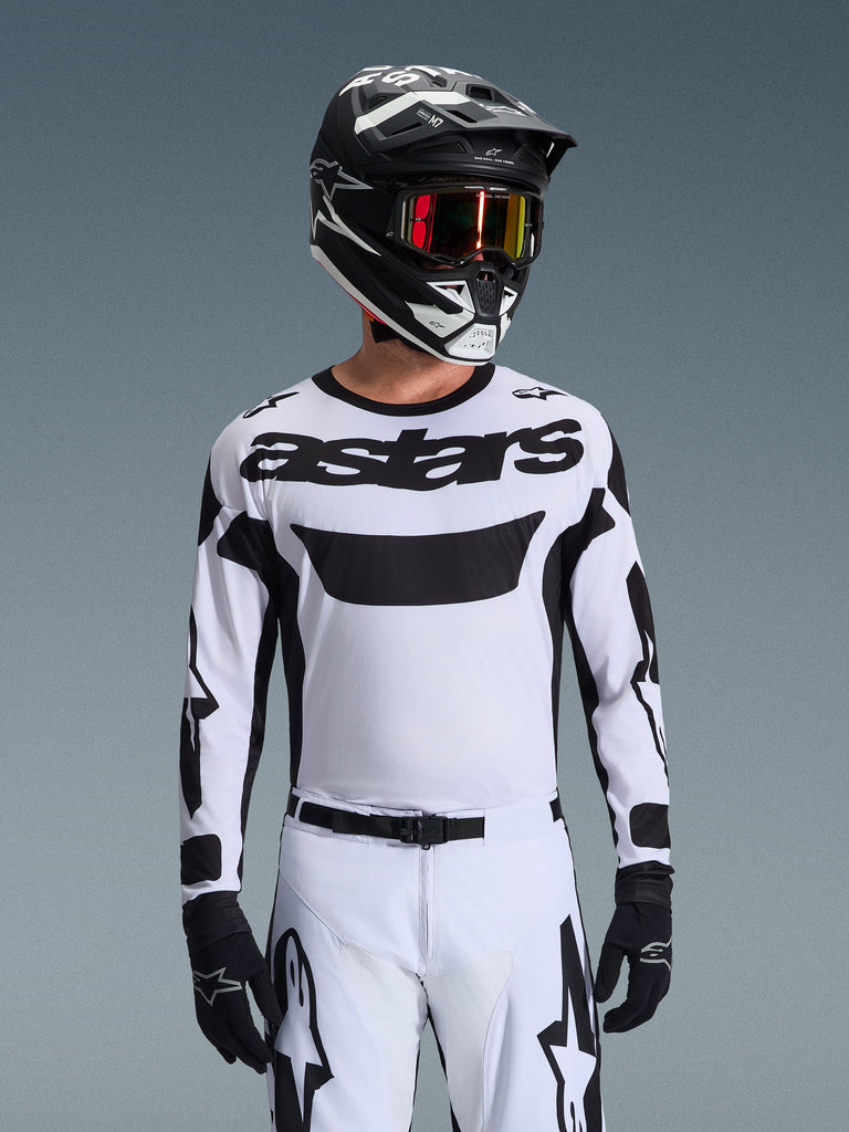 Motocross rider wearing the Alpinestars 2026 Racer Riway Jersey in White and Black, featuring 'astars' branding on the chest, paired with matching white and black pants, a black helmet with goggles, and black gloves, coordinated kit for off-road racing