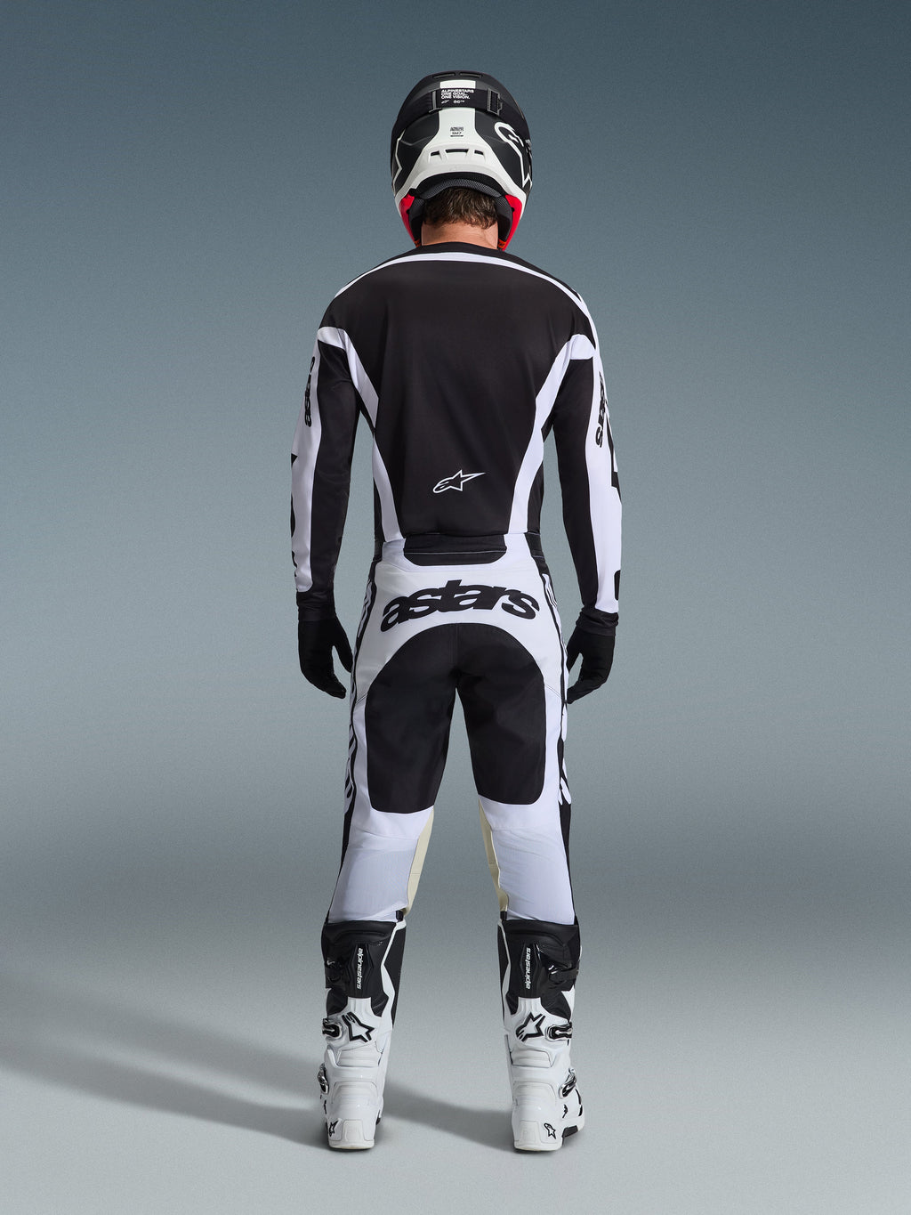 Motocross rider from the back wearing complete racing gear, 2026 Racer Riway Jersey in White and Black, matching pants with 'astars' branding on the seat, black helmet with white details, black gloves, and white and black boots, coordinated professional off-road outfit