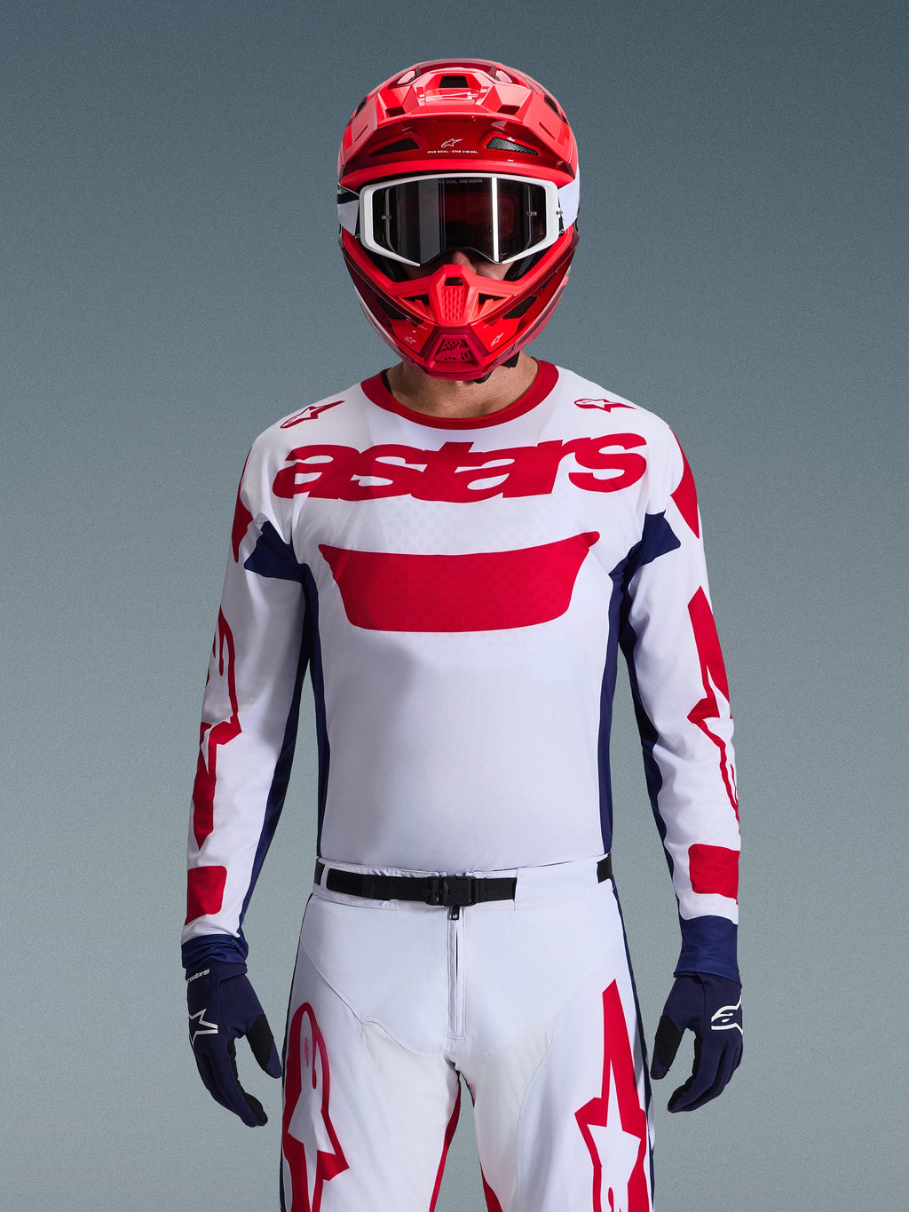 Ensemble Alpinestars Racer Riway 2026, pilote de motocross portant un maillot blanc avec logo rouge et accents bleu marine, pantalon blanc assorti avec graphismes rouges, casque rouge avec lunettes blanches, gants bleu marine, tenue de course tout-terrain professionnelle coordonnée.