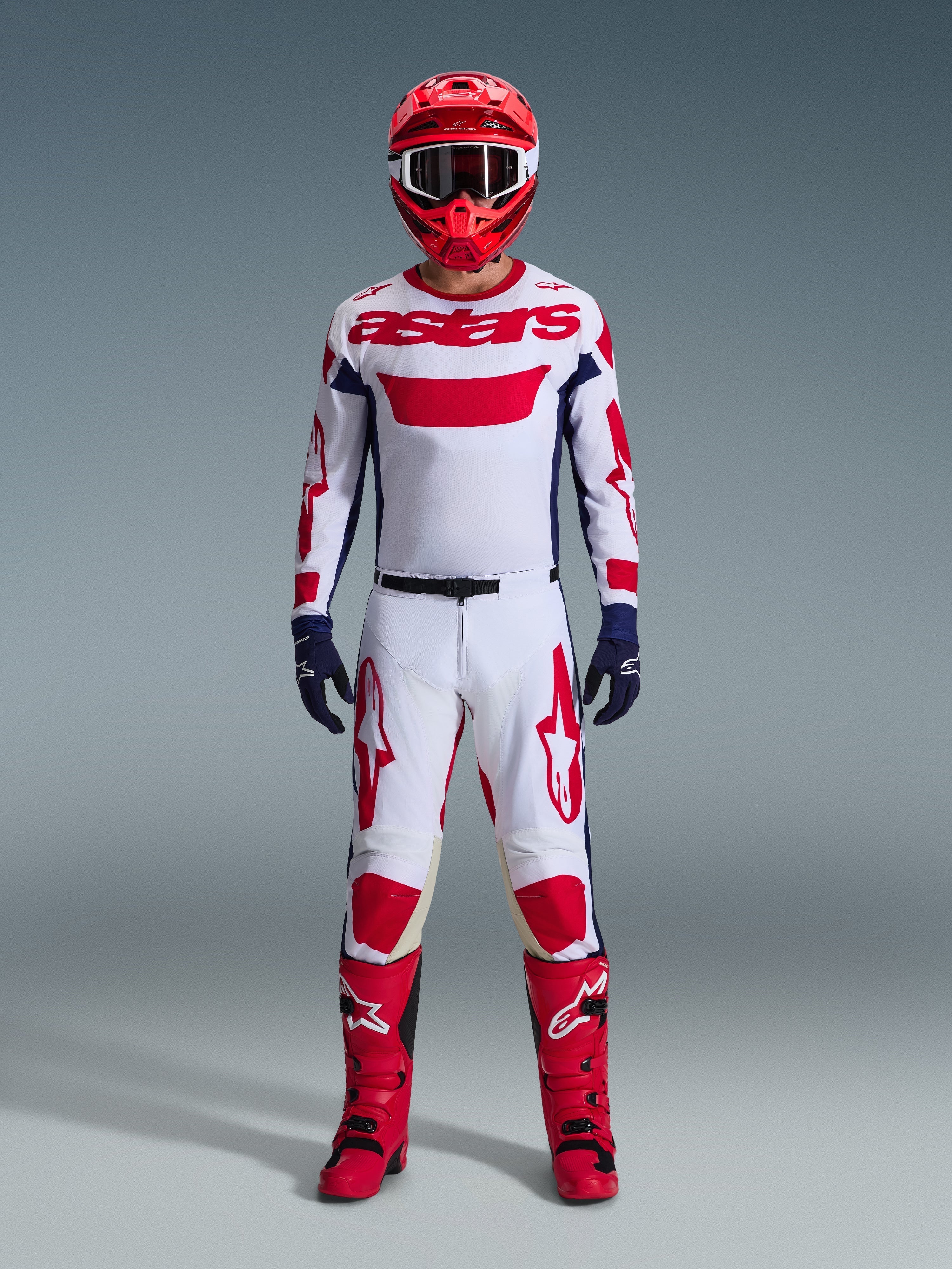 Motocross-Fahrer in kompletter Rennausrüstung, Alpinestars 2026 Racer Riway Trikot in Weiß Blau Rot, passender weiß-roter Hose, rotem Helm, roten Stiefeln und marineblauen Handschuhen, abgestimmtes Outfit für Offroad-Rennen