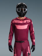 Motocross-Fahrer im Alpinestars 2026 Racer Riway Gear Set, Maroon und Pink, Trikot mit markantem rosa Branding auf der Brust, passende Hose mit schwarzen und rosa Akzenten, schwarzer Full-Face-Helm mit Goggles und schwarze Handschuhe, abgestimmtes Offroad-Rennoutfit.
