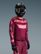 Motocross-Fahrer trägt Alpinestars 2026 Racer Riway Gear Set, burgunderrotes und pinkes Trikot mit markantem 'astars'-Branding, passende Hose mit pinken Akzenten, schwarzer Helm und Handschuhe, professionelles Rennoutfit für Offroad-Motocross
