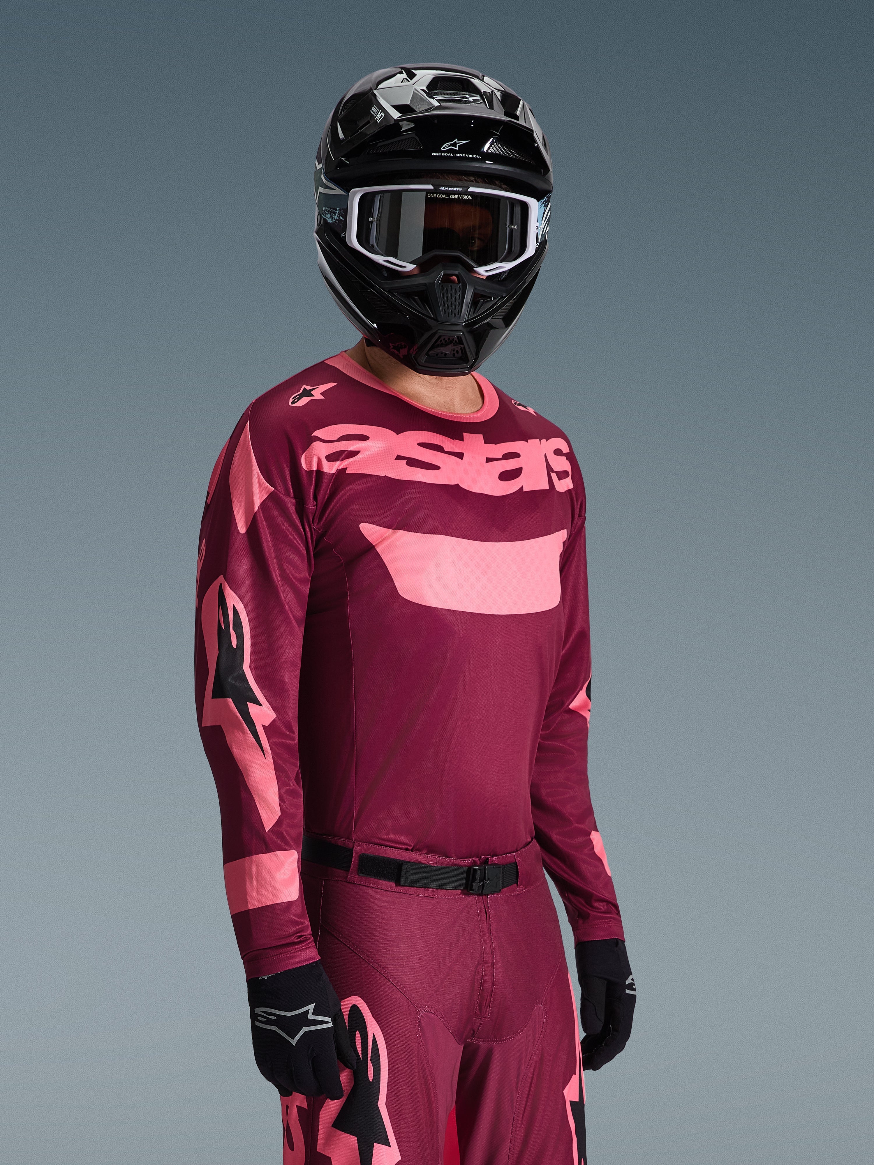 Motocross-Fahrer trägt Alpinestars 2026 Racer Riway Gear Set, burgunderrotes und pinkes Trikot mit markantem 'astars'-Branding, passende Hose mit pinken Akzenten, schwarzer Helm und Handschuhe, professionelles Rennoutfit für Offroad-Motocross