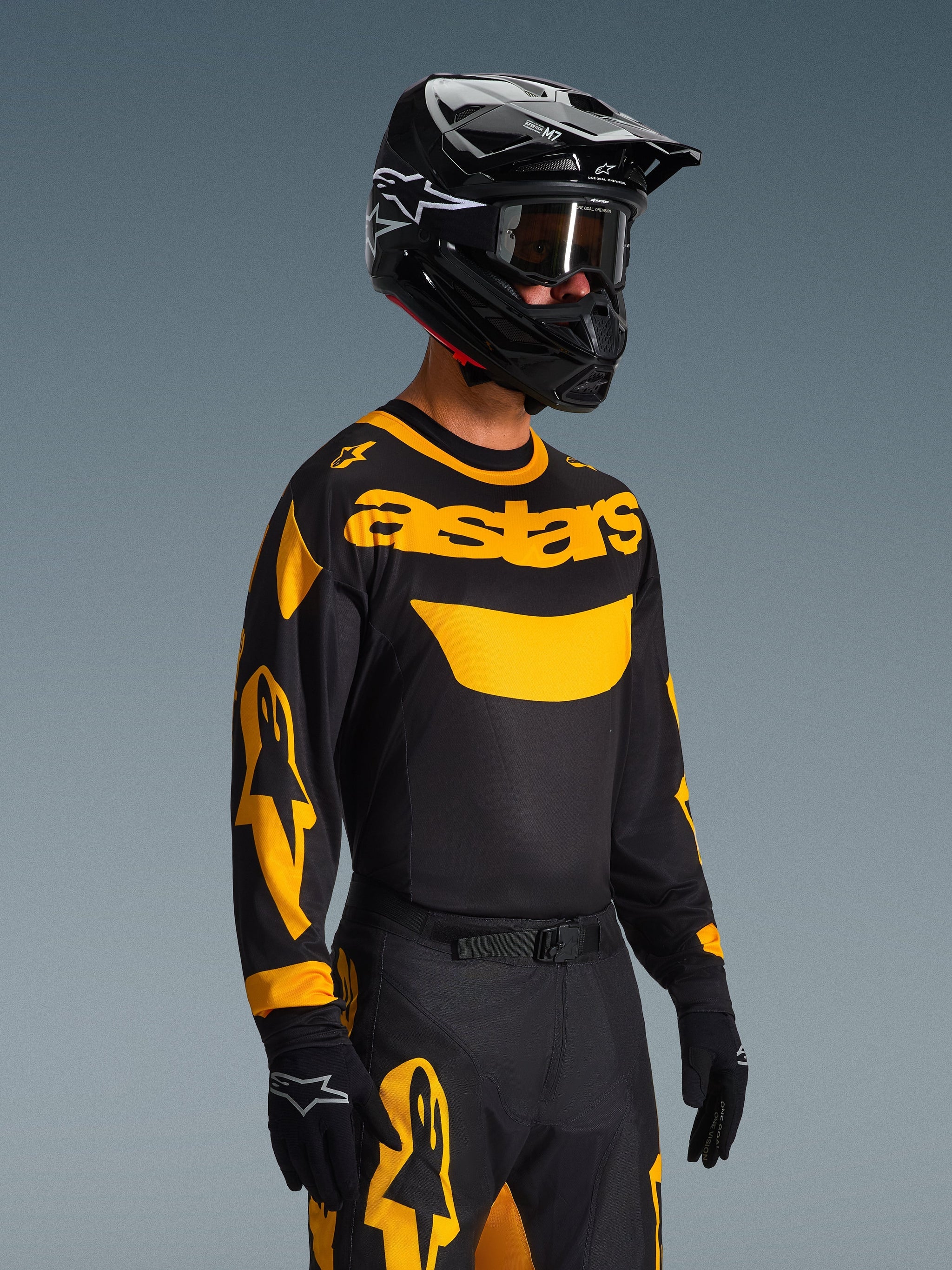 Pilote de motocross portant le maillot Alpinestars Racer Riway 2026 Jaune et Noir, maillot noir avec marquage 'astars' jaune vif et graphismes sur les manches, pantalon assorti noir et jaune, casque noir avec lunettes et gants noirs, tenue de course tout-terrain professionnelle