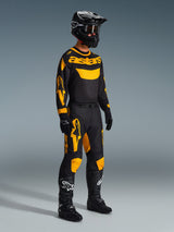 Pilote de motocross portant le maillot Racer Riway 2026 en jaune et noir, tenue de course complète avec pantalon assorti, casque, gants et bottes noirs, conçu pour la performance tout-terrain avec des graphismes Alpinestars audacieux.