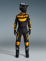 Pilote de motocross portant le maillot Racer Riway 2026 jaune et noir, coordonné avec un pantalon assorti, un casque noir et des bottes noires avec des logos Alpinestars blancs, équipement complet pour la course tout-terrain.