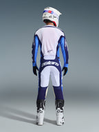 Rückansicht eines Motocross-Fahrers mit dem Alpinestars 2026 Racer Riway Trikot und der Hose in Ucla Blau und Weiß, ergänzt durch einen weißen Helm, schwarze Handschuhe und weiße Motocross-Stiefel, Hochleistungsausrüstung für Offroad-Rennen