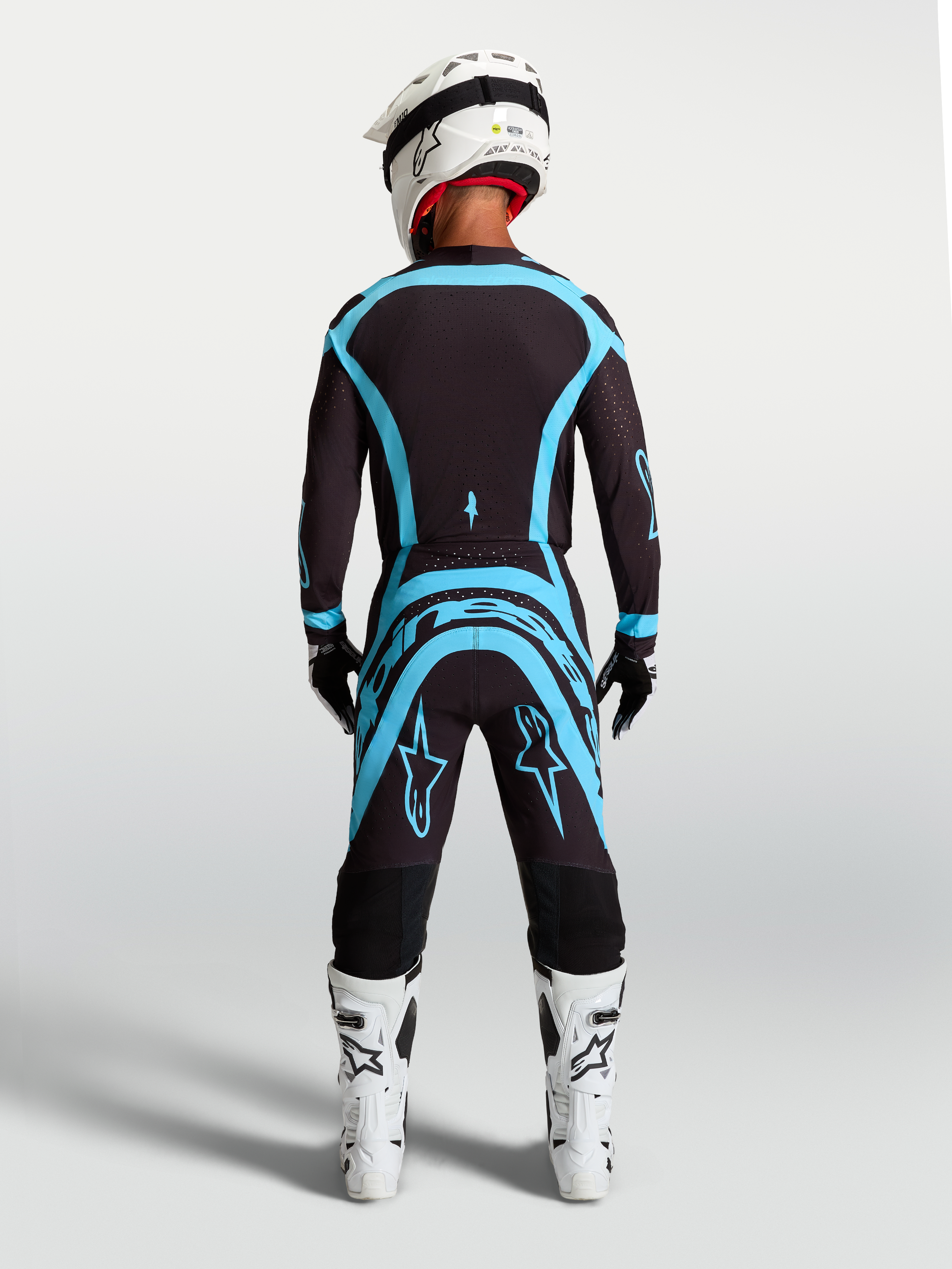 Alpinestars Supertech Vesta uitrustingsset voor motorcross, jersey en broek in zwart en turquoise, achteraanzicht, atletische racepasvorm.