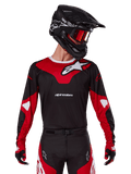 Alpinestars 2025 Racer Veil Jersey, motorcross jersey, zwart en felrood, gedragen met bijpassende broek, zwarte helm en rode crossbril, voorzien van opvallende witte logo's en een strak race-ontwerp, hoogwaardige uitrusting voor off-road motorcross