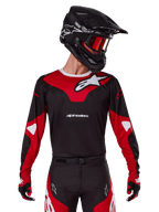 Alpinestars 2025 Racer Veil Jersey, motorcross jersey, zwart en felrood, gedragen met bijpassende broek, zwarte helm en rode crossbril, voorzien van opvallende witte logo's en een strak race-ontwerp, hoogwaardige uitrusting voor off-road motorcross