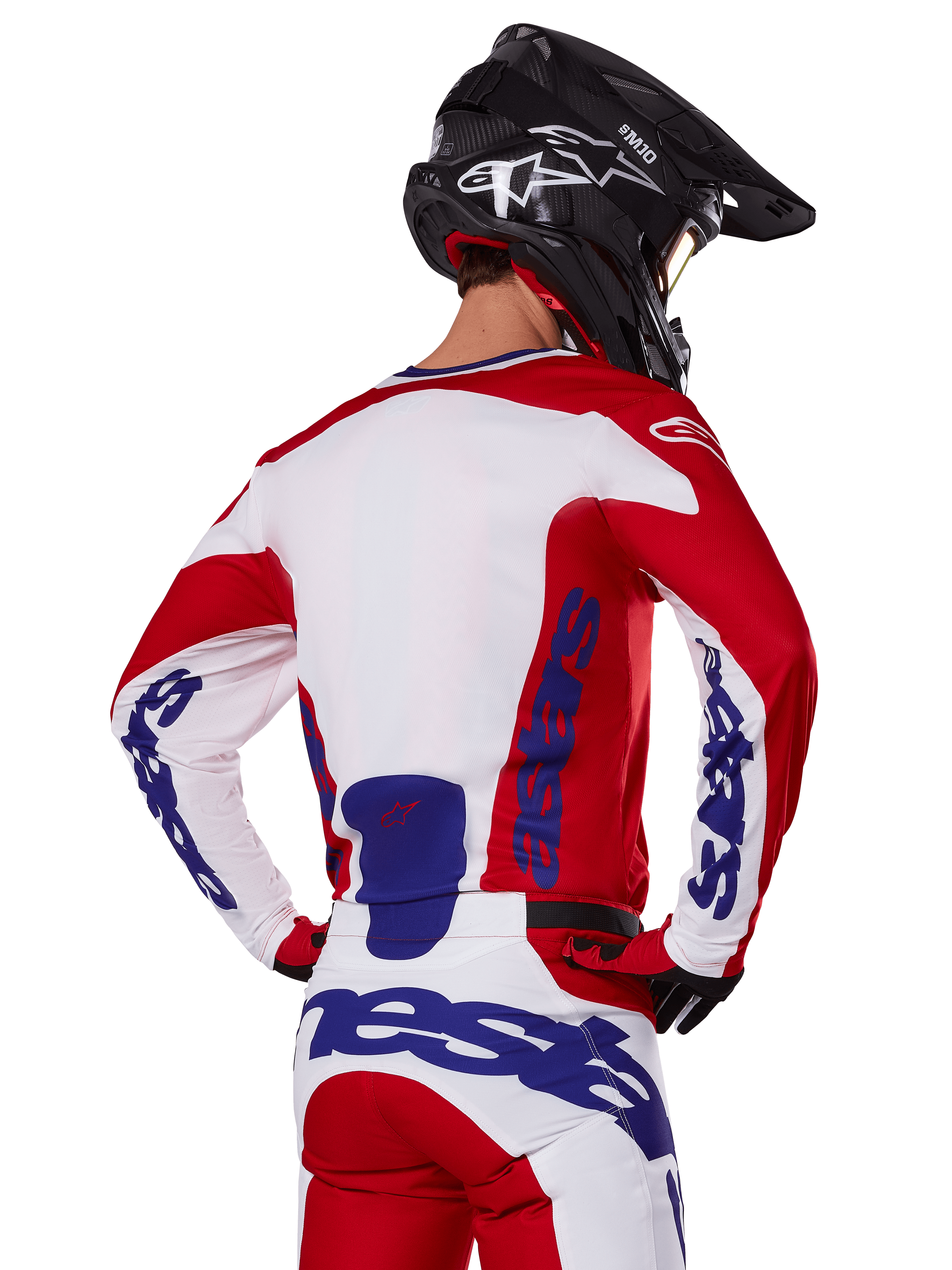 Alpinestars 2025 Racer Veil Jersey en broek, motorcross kledingset, helder rood, wit en blauw, achteraanzicht van rijder met bijpassende uitrusting en zwarte motorcrosshelm, voorzien van opvallende blauwe Alpinestars-branding, technische off-road racekleding.