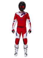 Motorcrossrijder in de Alpinestars 2025 Racer Veil Gear Set, felrood en wit jersey en broek met blauwe accenten, zwarte helm met rode bril, witte laarzen en rood-zwarte handschoenen, gecoördineerde outfit voor off-road racen