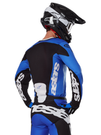 Alpinestars 2025 Racer Veil Gear Set, motorcrossuitrusting, blauw, zwart en wit, achteraanzicht van rijder die jersey en broek draagt met opvallende merklogo's, zwart-witte helm, gecoördineerde outfit voor off-road racen