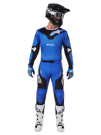 Motocrossrijder die de Alpinestars 2025 Racer Veil Gear Set draagt, blauw-zwarte jersey met bijpassende broek, zwarte helm met witte crossbril, witte en zwarte laarzen, gecoördineerde race-outfit voor off-road motorcross.