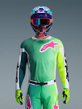 Maillot Alpinestars Racer Portl 2026, maillot de motocross, vert, blanc et noir avec un grand logo Alpinestars rose sur la poitrine, porté par un pilote avec un casque multicolore éclatant et des lunettes assorties, équipement de course tout-terrain professionnel