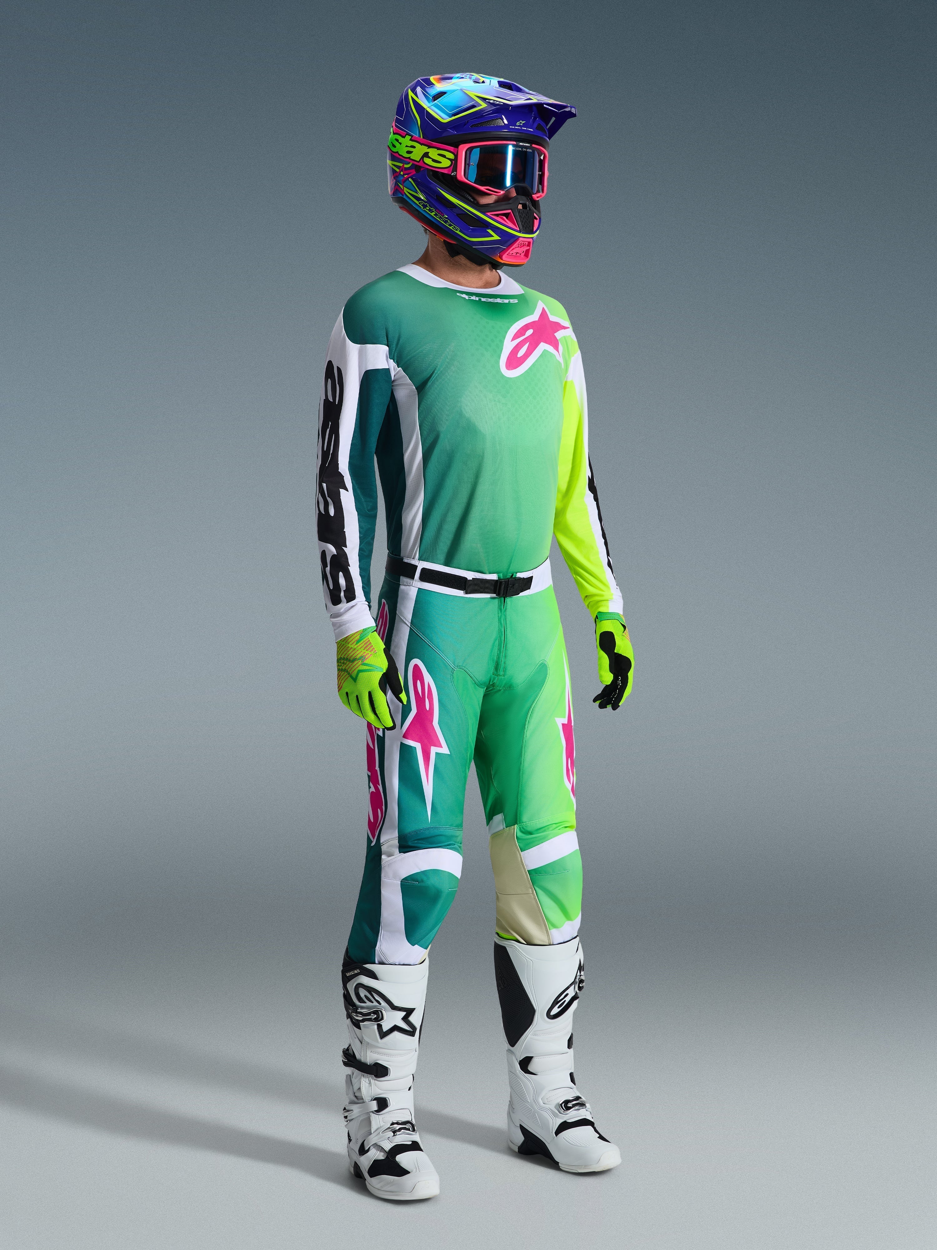 Motorcrossrijder in volledige race-uitrusting, 2026 Racer Portl Jersey in het groen met witte en zwarte mouwen en roze logo, bijpassende groene broek met roze accenten, veelkleurige helm met crossbril, wit-zwarte laarzen en groene handschoenen, gecoördineerde outfit voor off-road racing