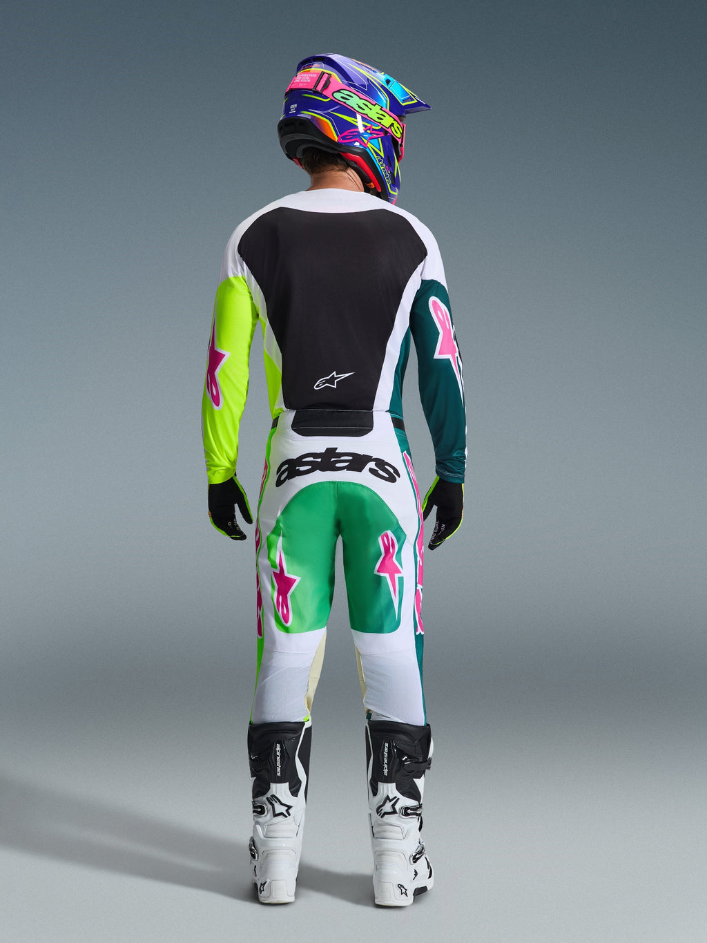 Motorcrosser van achteren gezien in de 2026 Racer Portl Jersey in Green White Black, voorzien van een zwart rugpaneel en asymmetrische groene mouwen met roze ster-logo's, gecombineerd met een bijpassende motorcrossbroek en witte laarzen.