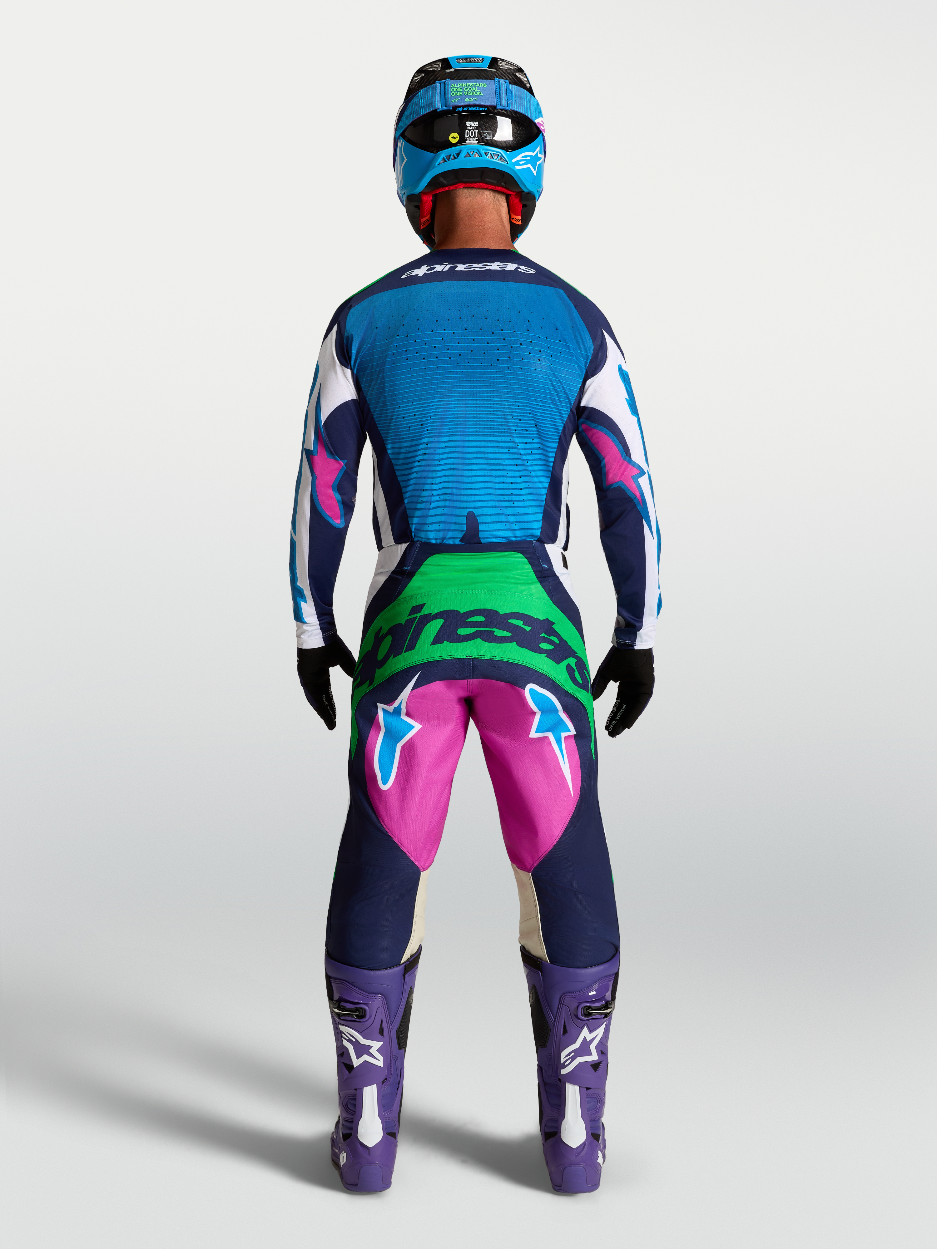 Alpinestars Techstar Maven jersey, heren motocross-uitrusting, blauw en marineblauw, achteraanzicht met lasergesneden ventilatie, gedragen door model met bijpassende broek en paarse laarzen.