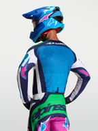 Alpinestars Techstar Maven Jersey, motocross performance heren-jersey, blauw en groen met roze accenten, achteraanzicht op model met verlengde achterkant en atletische racepasvorm.