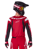 Alpinestars 2025 Fluid Haul Trikot, Motocross-Trikot, Hellrot und Schwarz, getragen als Teil eines kompletten Ausrüstungssets mit passender Hose und Handschuhen, schwarzer Helm mit gelb getönter Brille, weißes Branding und Logos, Hochleistungs-Offroad-Rennbekleidung
