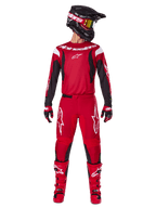 Alpinestars 2025 Fluid Haul Gear Set, Motocross-Outfit in hellem Rot und Schwarz, bestehend aus einem roten Trikot mit schwarzen Ärmeln und weißem Branding, passender roter Hose mit weißen Stern-Logos, schwarzem Helm mit gold getönter Brille und roten Stiefeln, komplette Ausrüstung für den Offroad-Sport