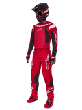 Pilote de motocross portant l'ensemble Alpinestars Fluid Haul 2025, rouge vif avec des accents noirs et blancs, tenue complète comprenant maillot, pantalon, casque, bottes et gants, conçue pour la performance et la protection en tout-terrain