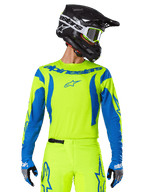 Alpinestars 2025 Fluid Haul Jersey, motorcross shirt, neongeel en blauw, met blauwe Alpinestars-branding op de borst, gedragen met bijpassende uitrusting waaronder een zwarte helm en blauwe handschoenen, atletische pasvorm voor off-road rijden