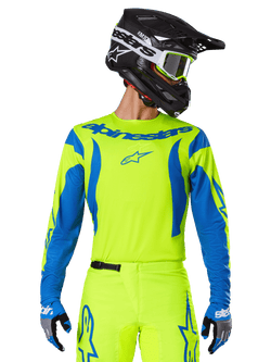 Alpinestars 2025 Fluid Haul Jersey, motorcross shirt, neongeel en blauw, met blauwe Alpinestars-branding op de borst, gedragen met bijpassende uitrusting waaronder een zwarte helm en blauwe handschoenen, atletische pasvorm voor off-road rijden