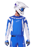 Alpinestars 2025 Fluid Haul Jersey, maillot de motocross bleu et blanc, porté avec un pantalon et des gants assortis, casque blanc avec lunettes bleues, ensemble d'équipement MX coordonné pour le tout-terrain