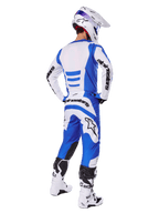 Pilote de motocross de dos portant l'ensemble d'équipement Alpinestars Fluid Haul 2025, maillot bleu et blanc avec pantalon assorti, casque blanc avec accents bleus et bottes de course blanches et noires, tenue de course tout-terrain coordonnée