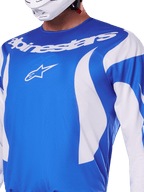 Maillot Alpinestars Fluid Haul 2025, bleu et blanc, porté par un pilote avec un casque blanc, avec lettrage Alpinestars et logo A-star blancs, coupe athlétique, matière légère évacuant l'humidité pour le motocross et le tout-terrain