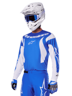 Motorcrosser draagt de Alpinestars 2025 Fluid Haul Gear Set in blauw en wit, met een blauwe jersey met witte accenten, bijpassende blauwe broek met sterlogo's, een witte helm met blauwe bril en gecoördineerde blauwe en grijze handschoenen, complete off-road race-outfit.