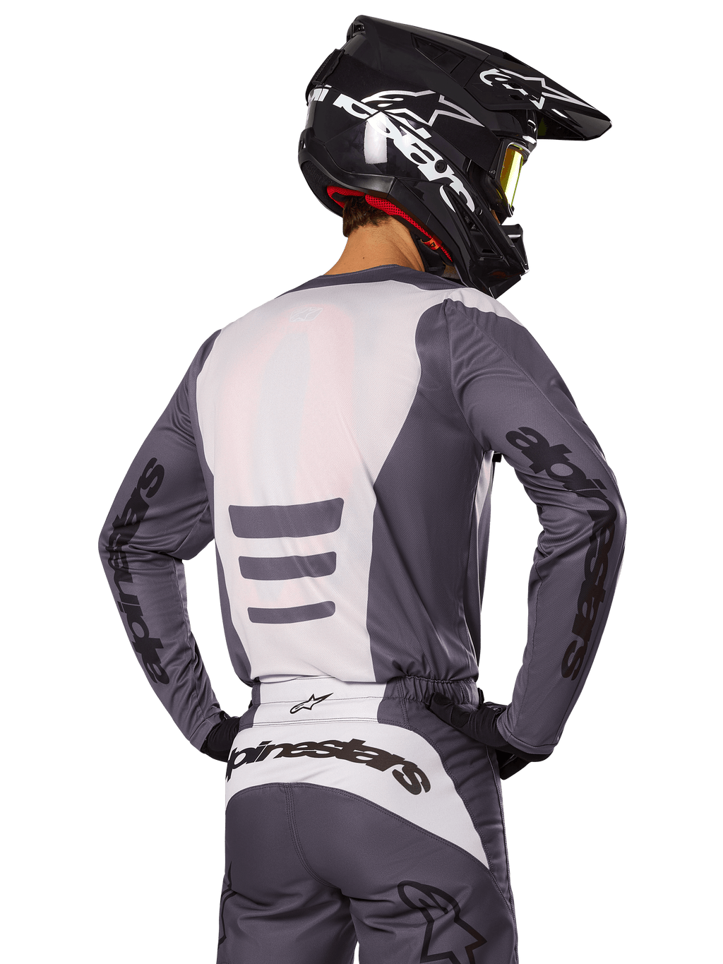 Motocrossrijder van achteren die de Alpinestars 2025 Fluid Haul Gear Set draagt, grijs en witte jersey en broek, zwarte helm met witte graphics, gele goggle, gecoördineerde motorcross race-outfit