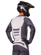 Motocrossrijder van achteren die de Alpinestars 2025 Fluid Haul Gear Set draagt, grijs en witte jersey en broek, zwarte helm met witte graphics, gele goggle, gecoördineerde motorcross race-outfit