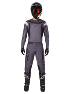 Alpinestars 2025 Fluid Haul Gear Set, motorcross uitrusting, grijs, grijze jersey en broek met zwarte accenten, zwarte helm met oranje bril, zwarte laarzen met witte logo's, gecoördineerde race-outfit voor off-road prestaties