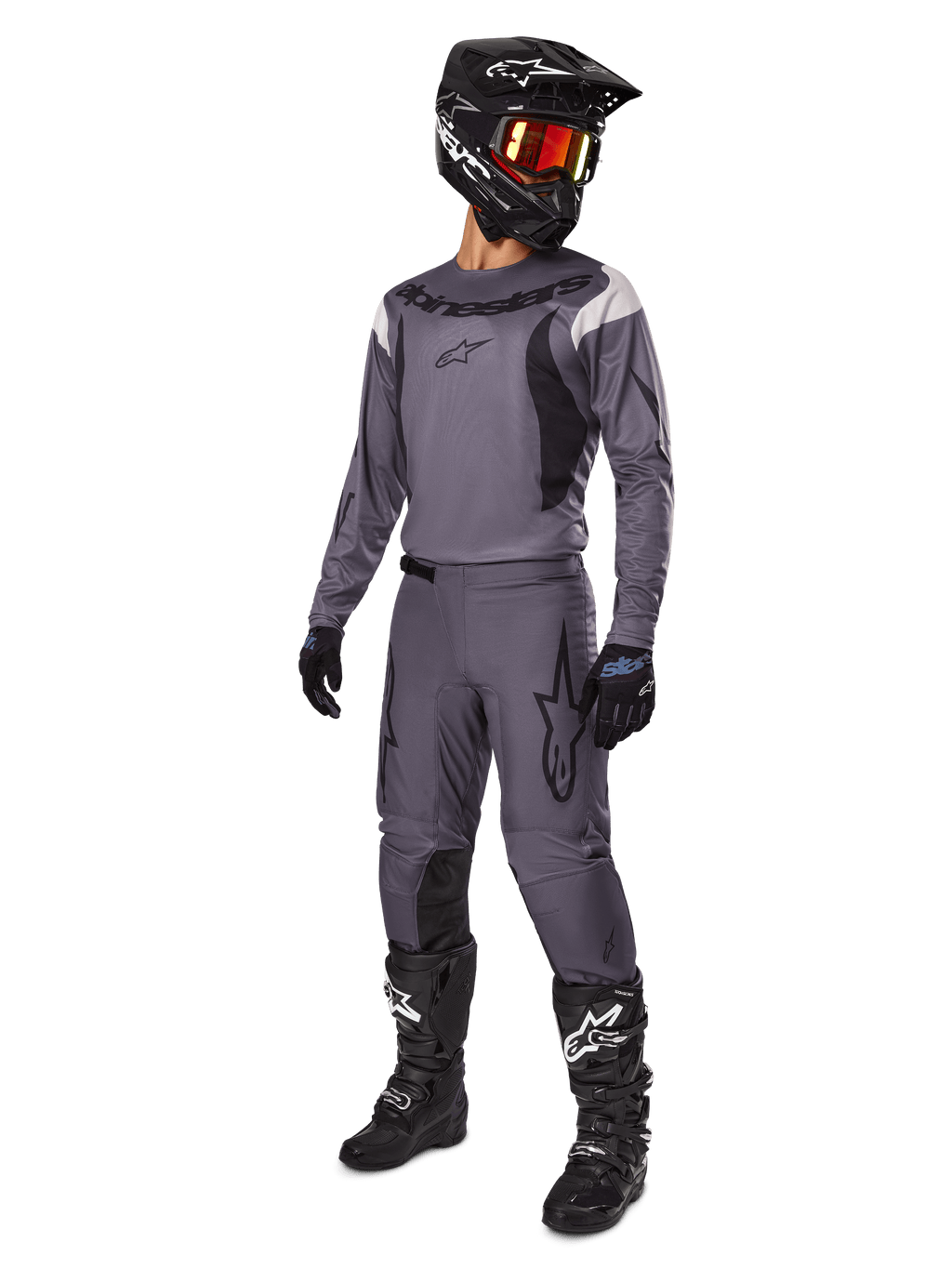 Motorcross rijder met Alpinestars 2025 Fluid Haul Gear Set in het grijs, inclusief grijze jersey en broek met zwarte accenten, zwarte helm met roodachtige bril, zwarte handschoenen en zwarte laarzen met witte logo's, complete off-road race-outfit
