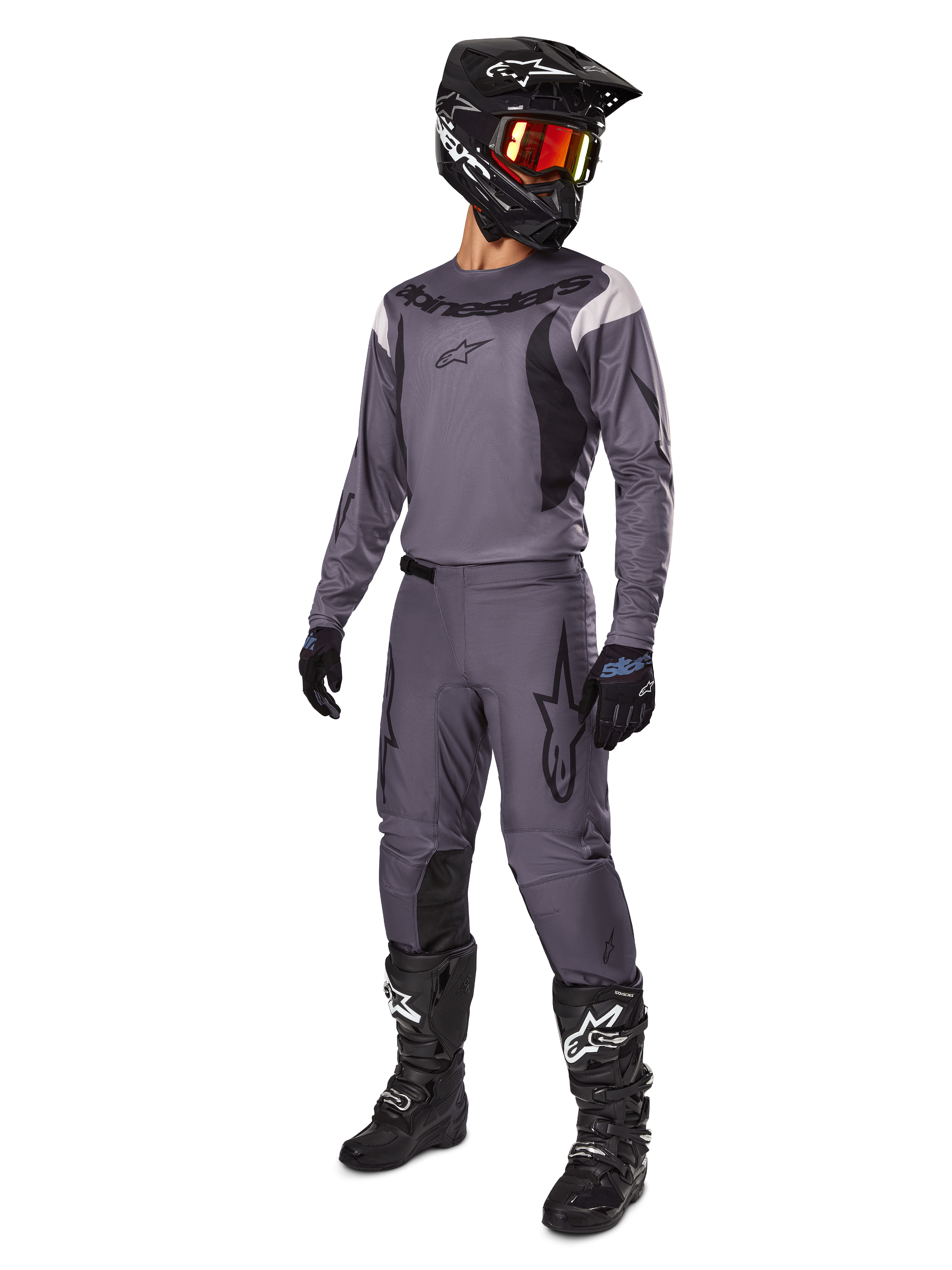 Motorcross rijder met Alpinestars 2025 Fluid Haul Gear Set in het grijs, inclusief grijze jersey en broek met zwarte accenten, zwarte helm met roodachtige bril, zwarte handschoenen en zwarte laarzen met witte logo's, complete off-road race-outfit