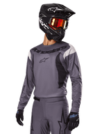Set d'équipement Alpinestars Fluid Haul 2025, maillot et pantalon de motocross gris avec accents noirs et blancs, porté avec un casque noir, des lunettes rouges et des gants noirs, coupe sportive athlétique pour la conduite tout-terrain