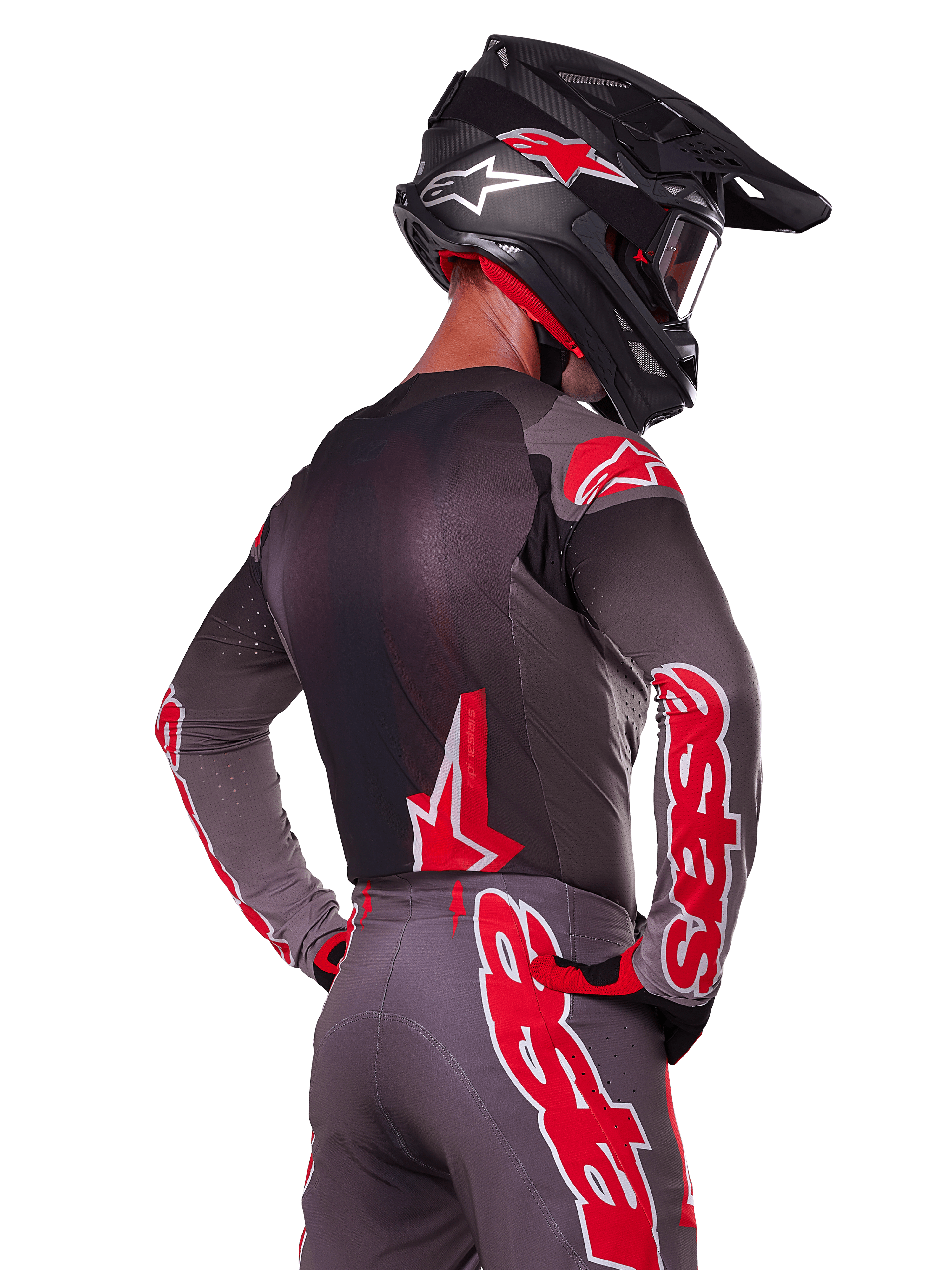 Ensemble d'équipement Supertech Lipan 2025 Alpinestars, pilote de motocross vu de dos, maillot et pantalon gris anthracite avec marquage 'astars' rouge vif sur les manches et le dos, complété par un casque noir